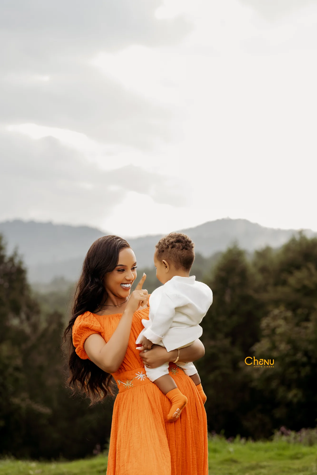 Gentle hillside playful moment with mother in orange dress and baby boy in white